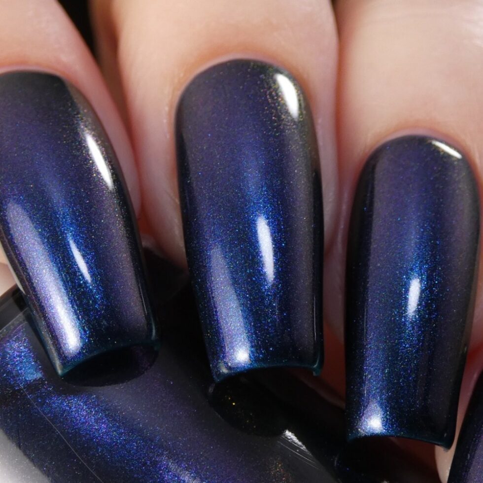 Close-up of nails adorned with PI Colors' "Judge None Choose One.000" Luxury Nail Lacquer, featuring an iridescent dark blue hue that captures light beautifully and evokes a subtle 90s nostalgia through its color shifts. The multichrome finish looks glossy and smooth, accentuating the polish's shimmer and depth.