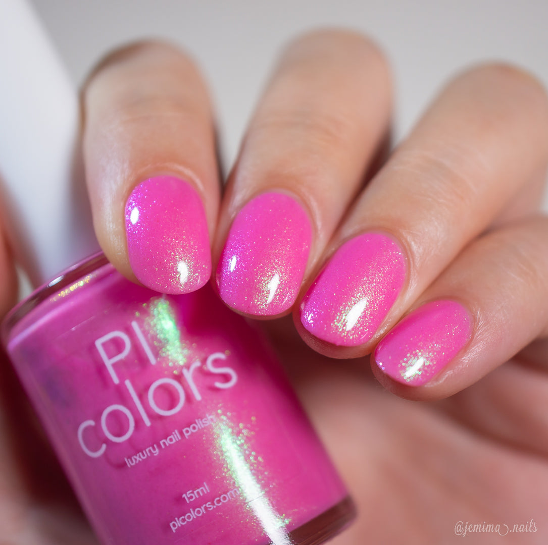 A hand with neatly manicured nails painted in "Mint and Summer.100" by PI Colors holds the matching bottle, the vibrant shade shining with a glittery finish that reflects light and showcases this handmade nail polish’s sparkling allure.