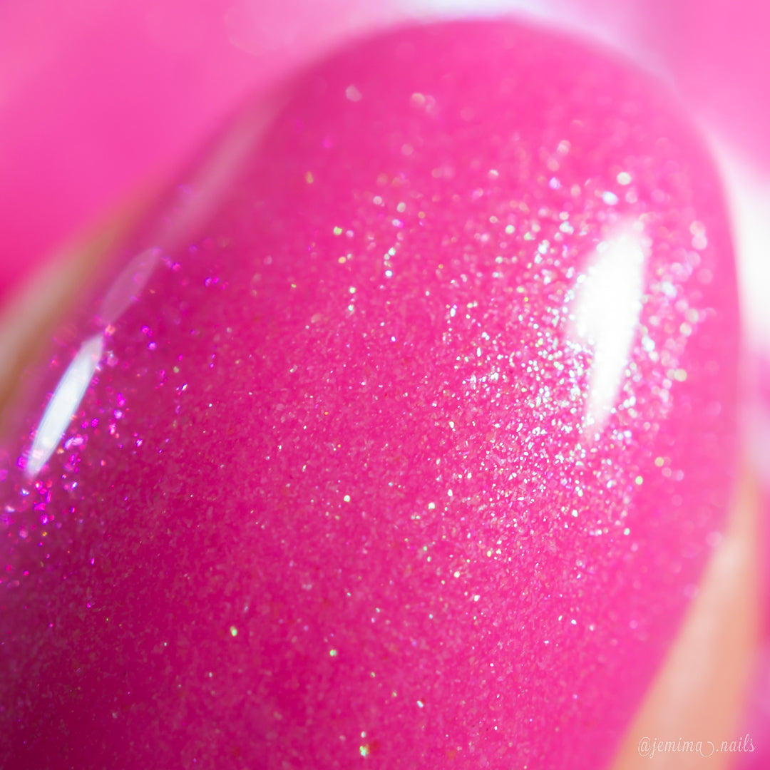A close-up of a fingernail painted with PI Colors Mint and Summer.100, featuring glossy, fluorescent pink polish with fine sparkles and a smooth, shiny finish highlighted by handmade colorshifting shimmer.