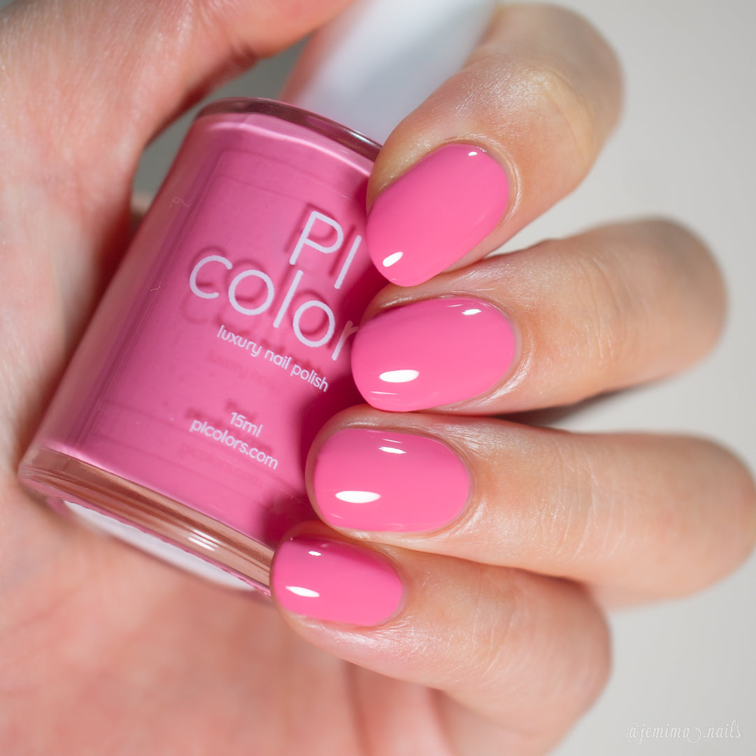 A hand holds a bottle of PI Colors "Neapolitan.432" pink nail polish, nails painted in the same glossy shade, beautifully manicured and displaying the PI Colors luxury nail lacquer label.