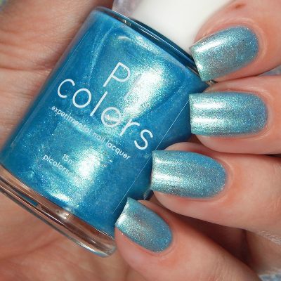 Close-up of a hand showcasing nails adorned with shimmering blue nail polish. A matching bottle of Loulaki.101 Blue Nail Polish from PI Colors is held between the fingers, labeled "PI Colors - Experimental Nail Lacquer." This handmade polish, enriched with iridescent flakies, features a metallic finish.