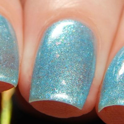 Close-up of polished fingernails with Loulaki.101 Blue Nail Polish by PI Colors, showcasing a shimmering blue shade. The nails reflect light, emphasizing their glossy finish and iridescent flakies for an enchanting look.