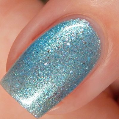 Close-up of a fingernail with PI Colors' Loulaki.101 Blue Nail Polish, showcasing its sparkly blue metallic shade with handmade iridescent flakies for a smooth, glossy finish. The fine glitter particles reflect light beautifully, allowing the skin around the nail to be subtly visible.