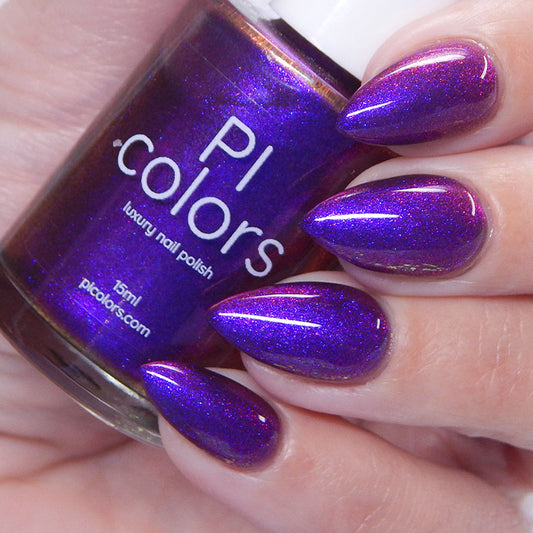 A hand with long, almond-shaped nails sports the vibrant shimmering purple of PI Colors' "Danbury Does It.000" from their Luxury Nail Lacquers. Held in the same hand, the bottle features a 10-free formula that marries elegance with nail care.