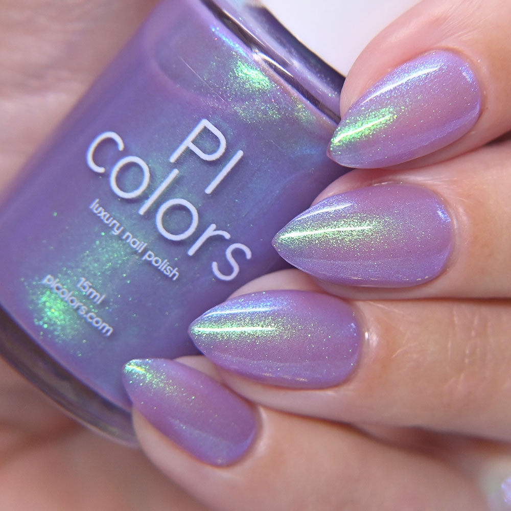 Purple nail polish with green glitter held by a hand, next to a bottle of PI Colors nail polish.