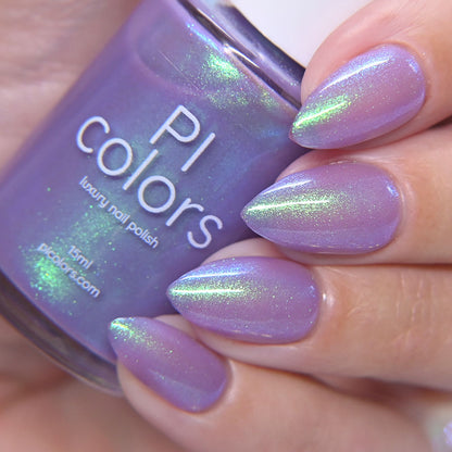 Purple nail polish with green glitter held by a hand, next to a bottle of PI Colors nail polish.
