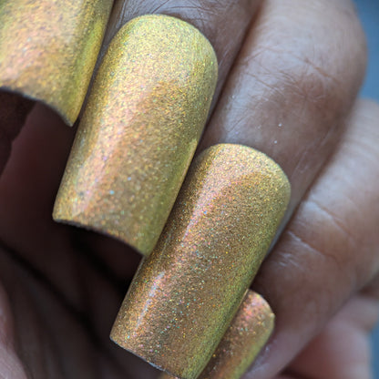 A close-up shot showcases a hand with fingers adorned in PI Colors' Golden Fuyuki.000, a luxurious metallic gold holo glitter nail polish. The polish delivers a shimmering effect, reflecting light in diverse shades of gold and bronze on neatly manicured and smooth nails.