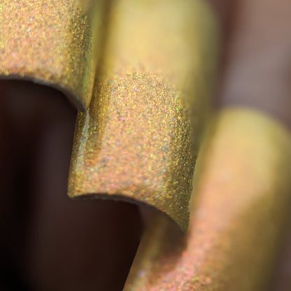 A close-up of the shimmering, curved surfaces of Golden Fuyuki.000 by PI Colors reveals a golden-brown hue with a textured, metallic finish. The image showcases the edges, emphasizing their smooth curves and sparkling details that resemble the luxurious effect of metallic gold holo glitter in nail polish under light.