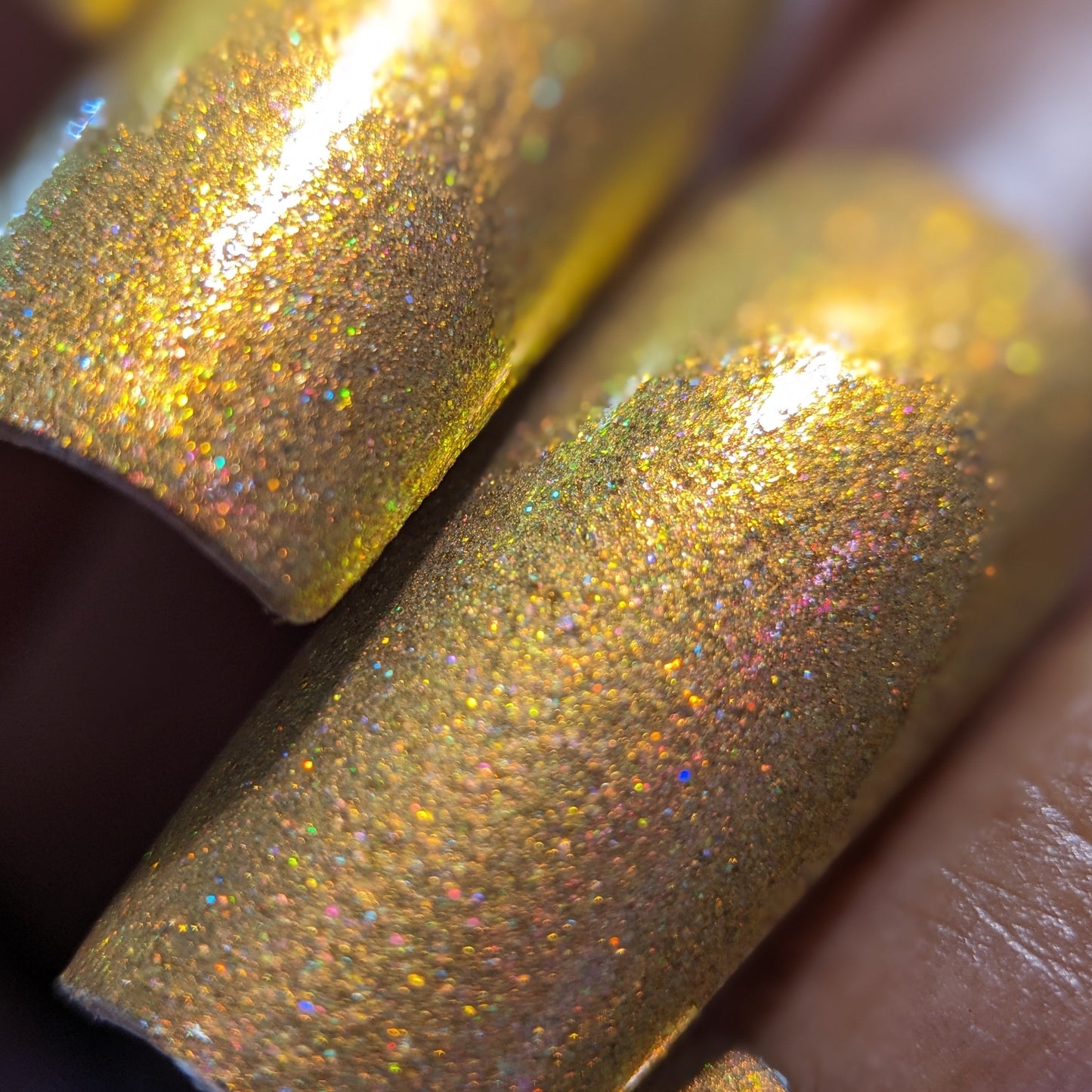 Close-up of a person's fingernails adorned with PI Colors' Golden Fuyuki.000, showcasing a luxurious holographic effect with metallic gold holo glitter. The image focuses on two nails, emphasizing their vibrant texture and glossy shine.