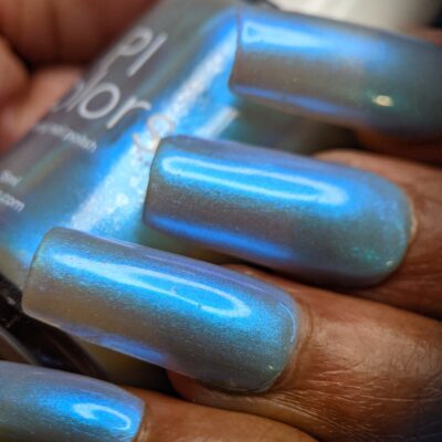 Close-up of long nails painted in the luxurious electric silver blue hue of PI Colors' Cloud Rainbow.303 Blue Nail Polish, reflecting light with a shimmering effect. The nails are positioned near a bottle of color-changing nail polish with a similar shade.