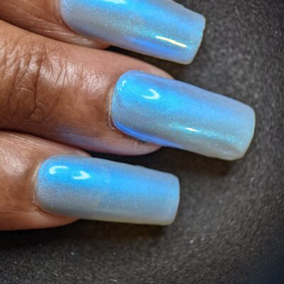 Close-up of a hand with long, square-shaped nails adorned in PI Colors' luxurious Cloud Rainbow.303 Blue Nail Polish, showcasing shimmering color-changing effects against a dark background.