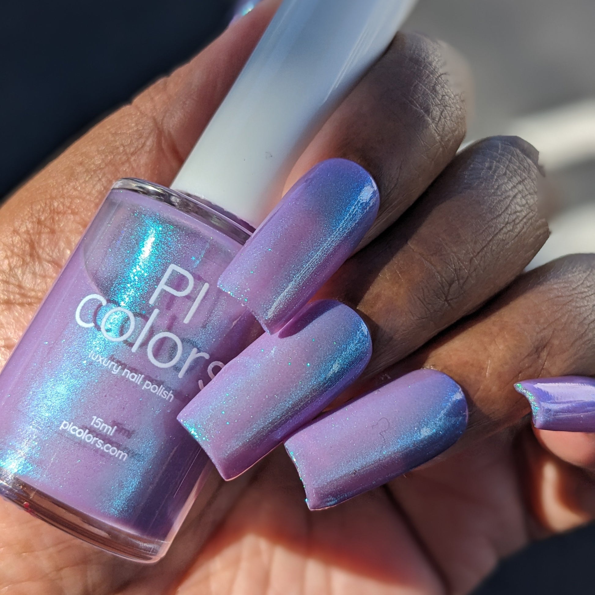 Hand with purple nail polish holding a bottle of PI colors nail polish.