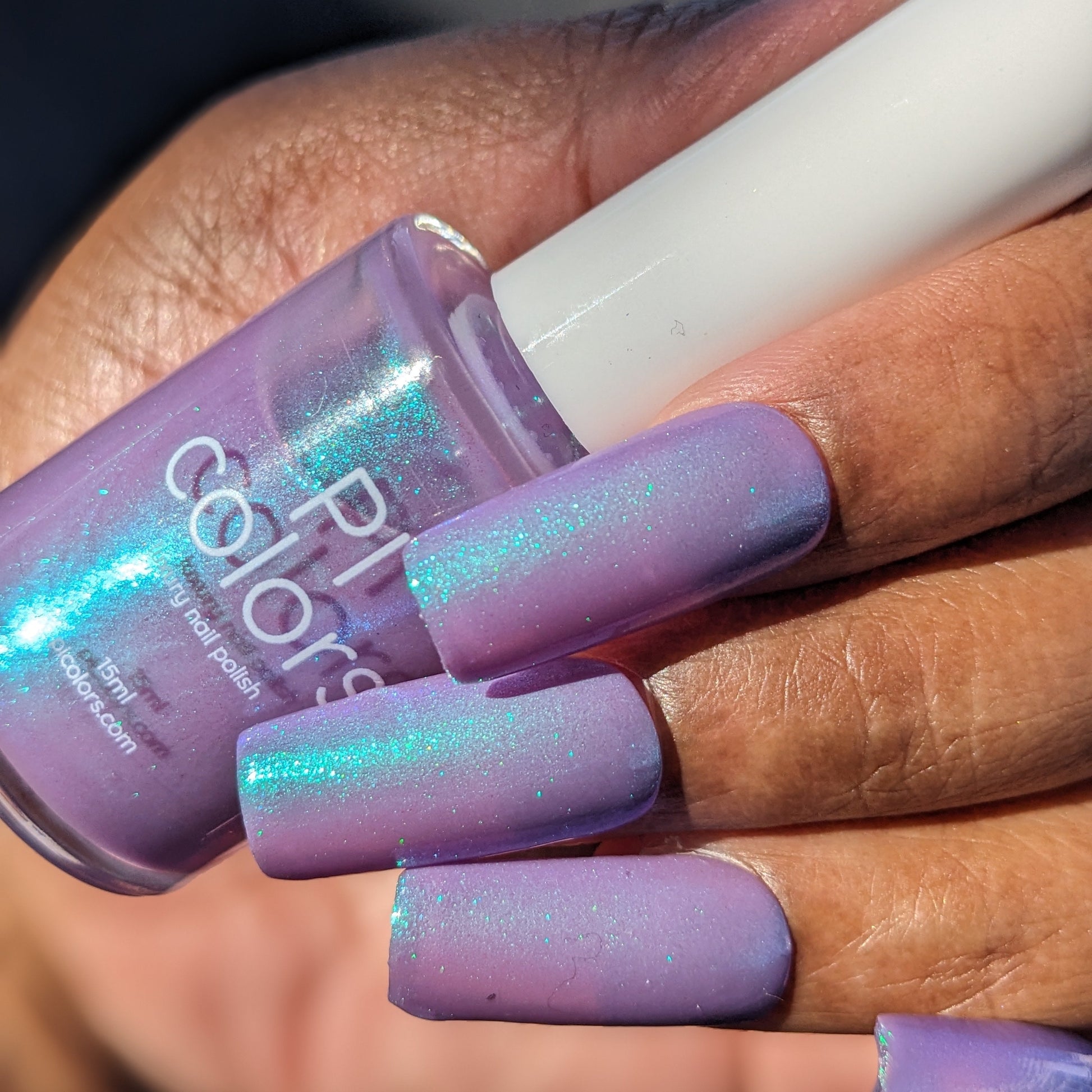 Purple nail polish bottle held by a hand with matching purple nails.