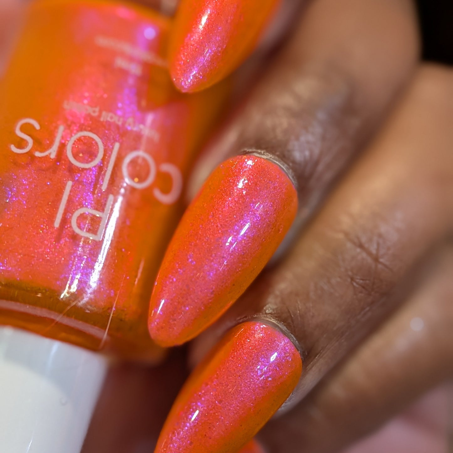 Nail polish bottle with bright orange nail polish on a hand