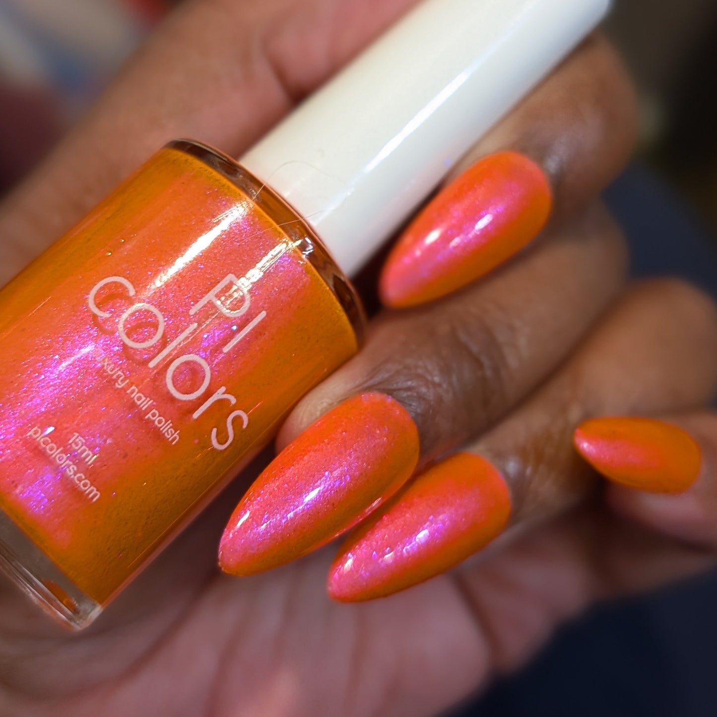 Hand holding a bottle of orange nail polish with matching nails.