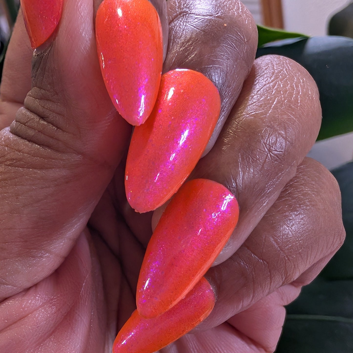 Hand with bright orange-pink nail polish on a blurred background