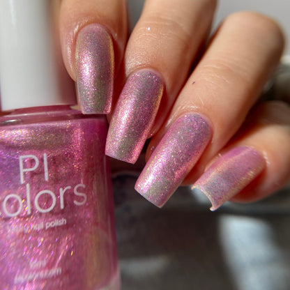 A close-up of a hand with fingernails painted in a shimmering pink nail polish, holding a bottle of PI colors nail polish with the same glittery pink shade.