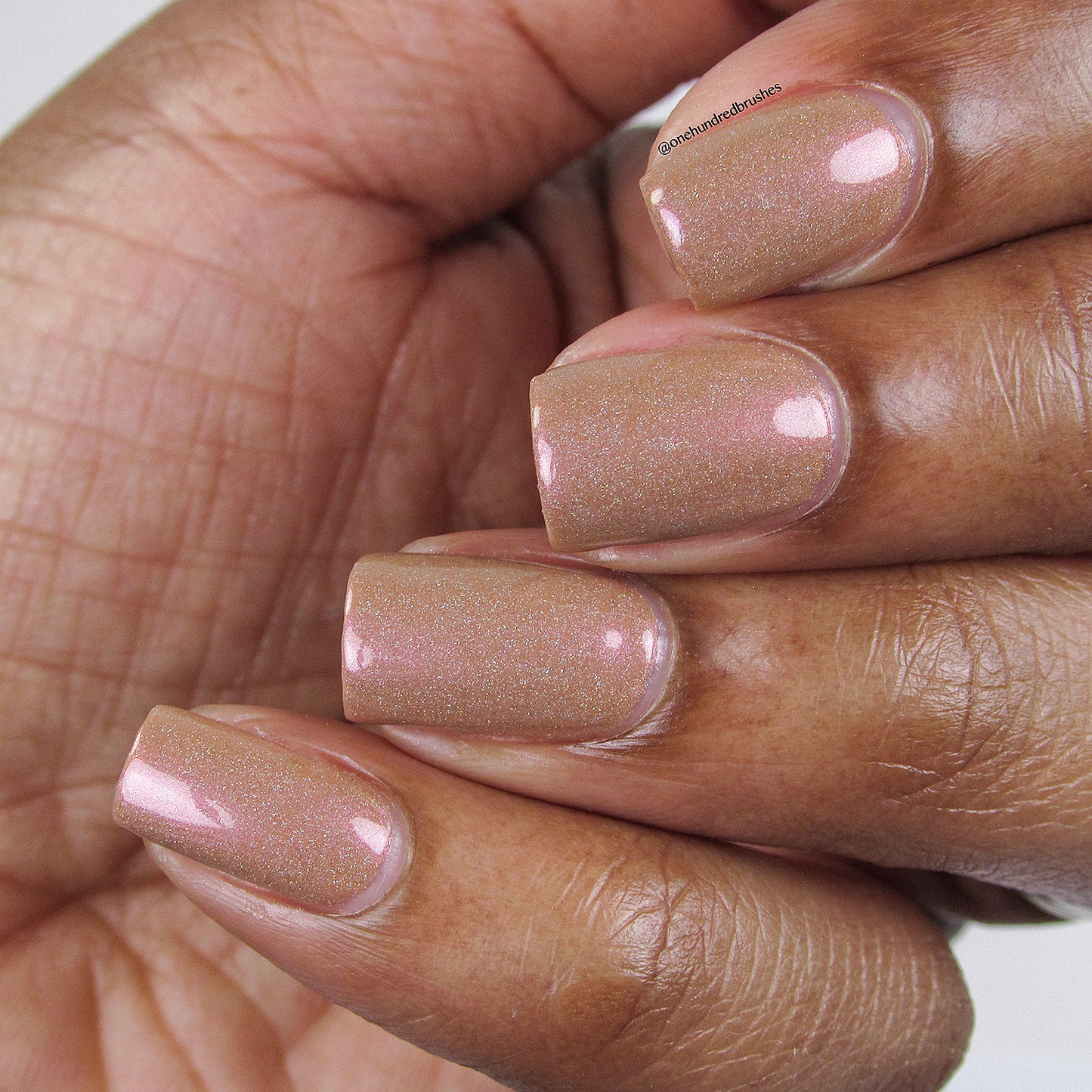 A close-up of a hand showcases neatly manicured nails, painted with Phoenix.087 Brown Nail Polish by PI Colors. The nails exhibit a shimmery, peachy-beige hue with a touch of holographic glitter, maintaining a well-shaped and glossy finish.