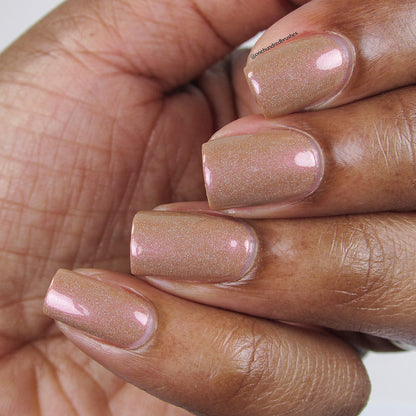 A close-up of a hand showcases neatly manicured nails, painted with Phoenix.087 Brown Nail Polish by PI Colors. The nails exhibit a shimmery, peachy-beige hue with a touch of holographic glitter, maintaining a well-shaped and glossy finish.