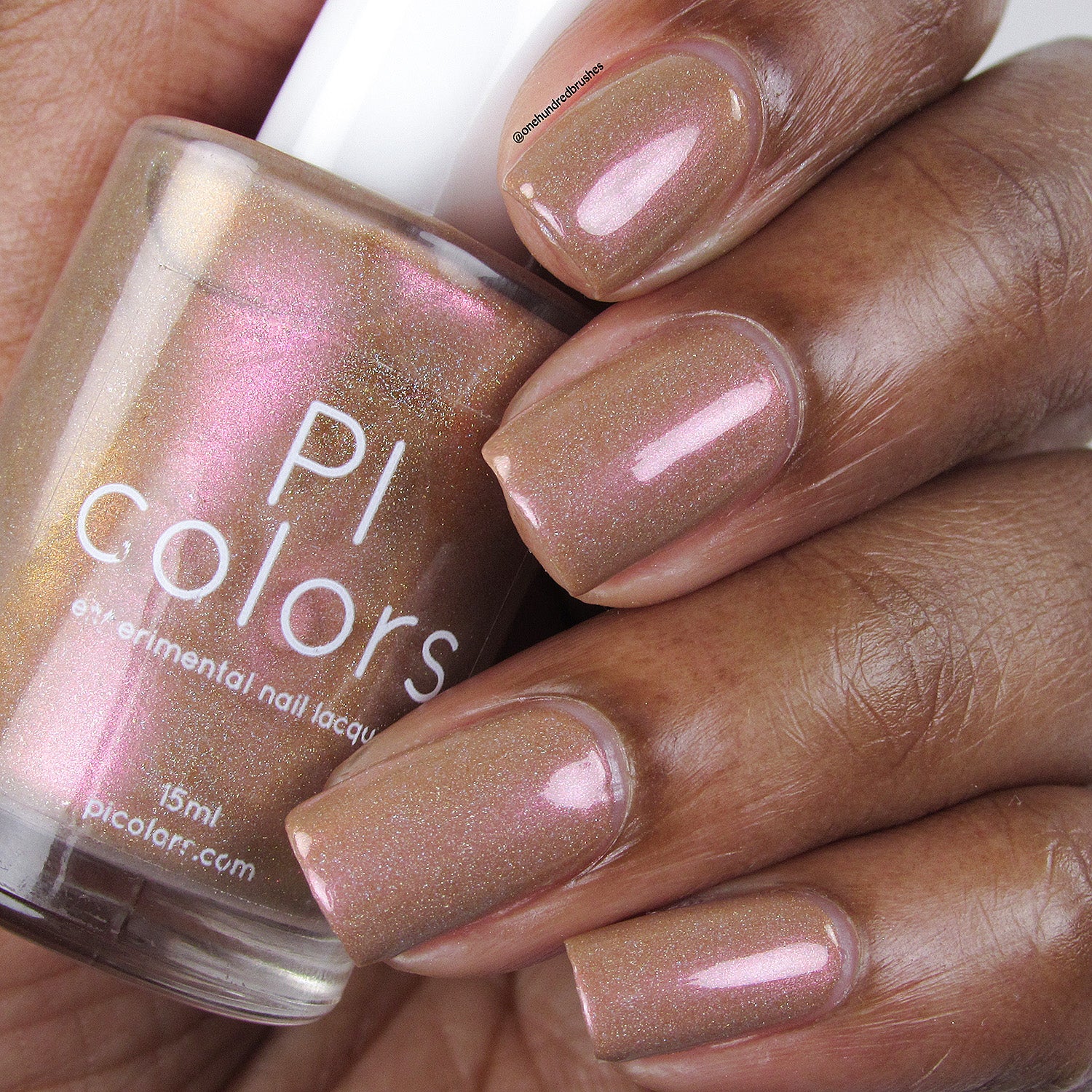 A hand with shimmering pinkish-brown nail polish, accented by holographic glitter, holds a bottle of PI Colors 10-free Phoenix.087 Brown Nail Polish in a matching enchanting shade.