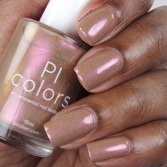 A hand with shimmering pinkish-brown nail polish, accented by holographic glitter, holds a bottle of PI Colors 10-free Phoenix.087 Brown Nail Polish in a matching enchanting shade.