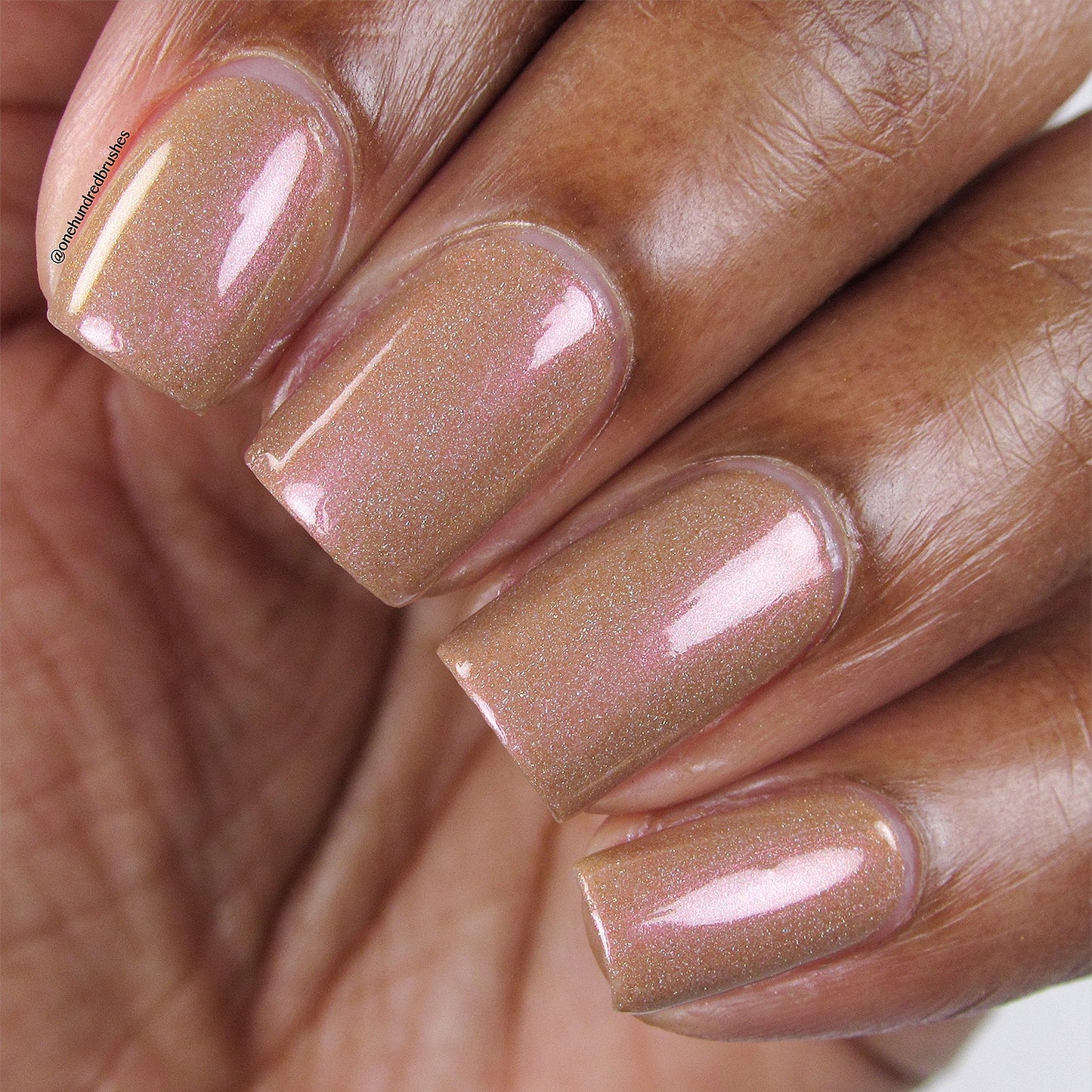 Close-up of a hand adorned with the peach-hued, shimmery Phoenix.087 Nail Polish by PI Colors on neatly manicured nails. The glossy finish reflects light, showcasing subtle sparkle against the rich, warm brown skin tone.