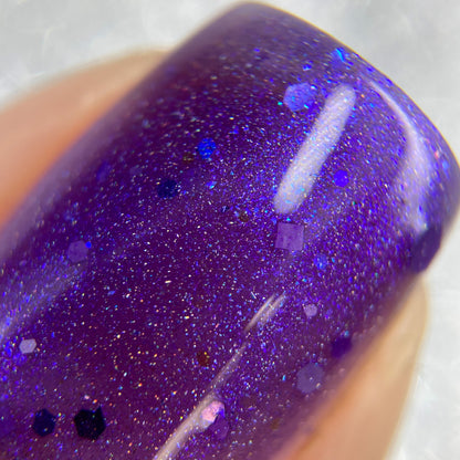 Close-up of a fingernail adorned with PI Colors' Purple Smoke.001 Purple Nail Polish. The glossy finish showcases holo purple glitters, creating a starry effect with specks of various sizes that reflect light beautifully.