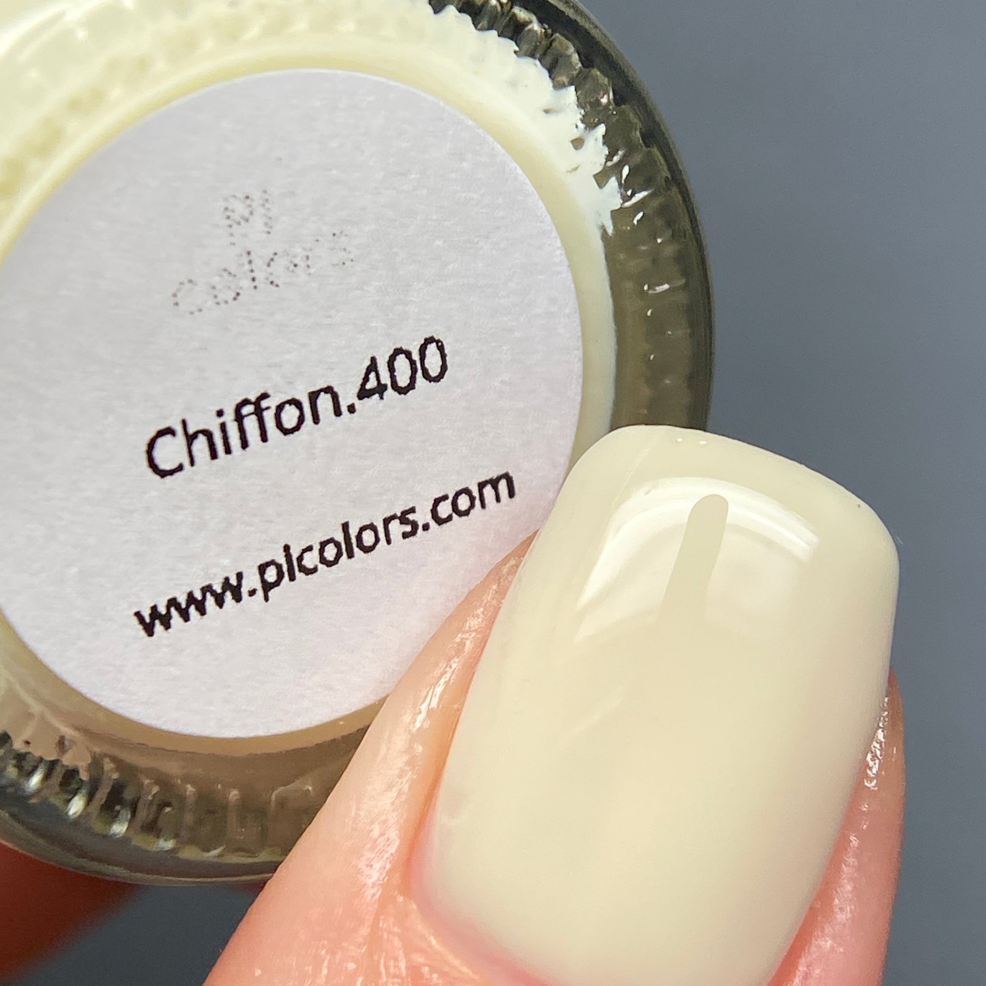 A close-up of a fingernail painted with a pale cream nail polish labeled "Chiffon.400" showcases PI Colors' Chiffon.400 Yellow Nail Polish, which features a chic creme finish. The nail polish bottle cap also hints at the website: www.picolors.com.