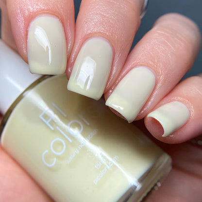 Close-up of a hand with fingers painted in glossy, pastel yellow nail polish, holding a bottle of PI Colors Chiffon.400 Yellow Nail Polish. The creme finish highlights the well-manicured nails against a blurred background.