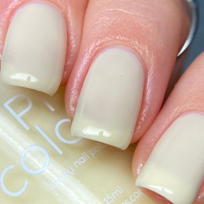 A close-up of a hand with neatly manicured fingernails painted in glossy, pastel yellow nail polish shows nails exhibiting a smooth and shiny creme finish, while the PI Colors Chiffon.400 Yellow Nail Polish bottle peeks out in the background.