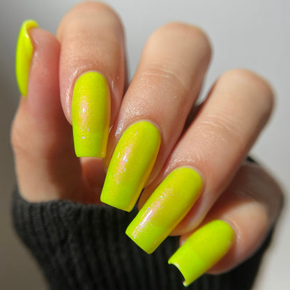 A close-up of a hand with long, square-shaped nails painted in a bright neon yellow-green glossy finish, wearing a dark ribbed sleeve against a light gray background.
