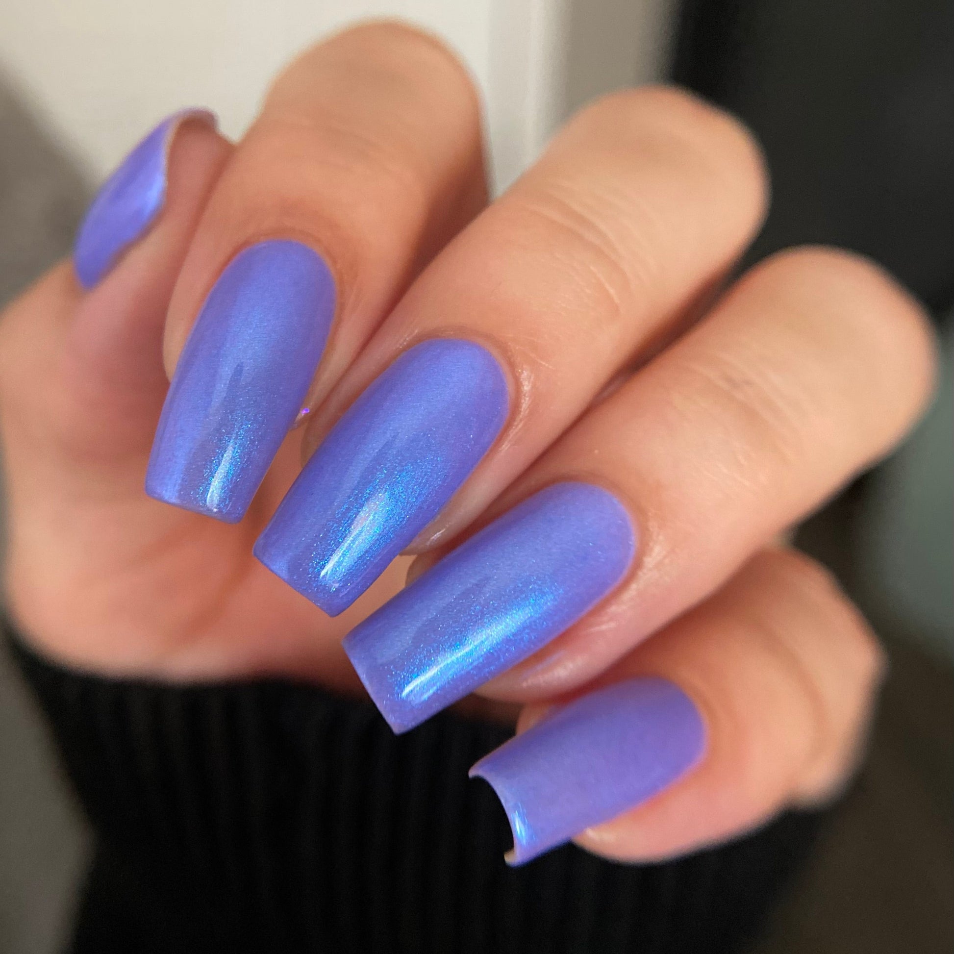 A close-up of a hand with long, almond-shaped nails painted in a glossy, shimmery periwinkle purple nail polish.