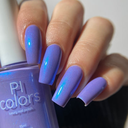 A close-up of a hand with long, glossy lavender-blue manicured nails holding a bottle of PL colors shimmering nail polish.