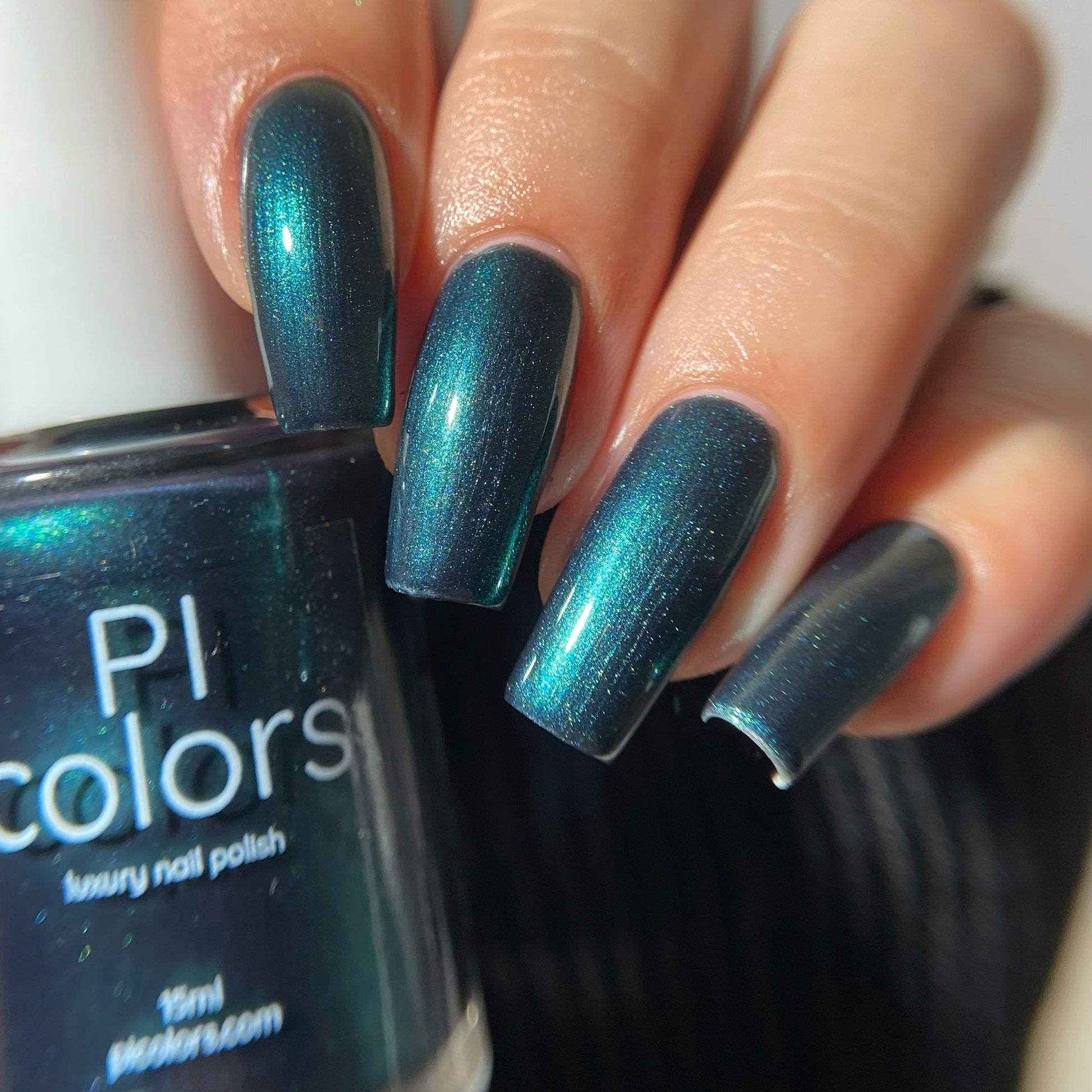 A close-up of a hand with fingernails painted in a metallic teal nail polish, holding a bottle of PI colors luxury nail polish.