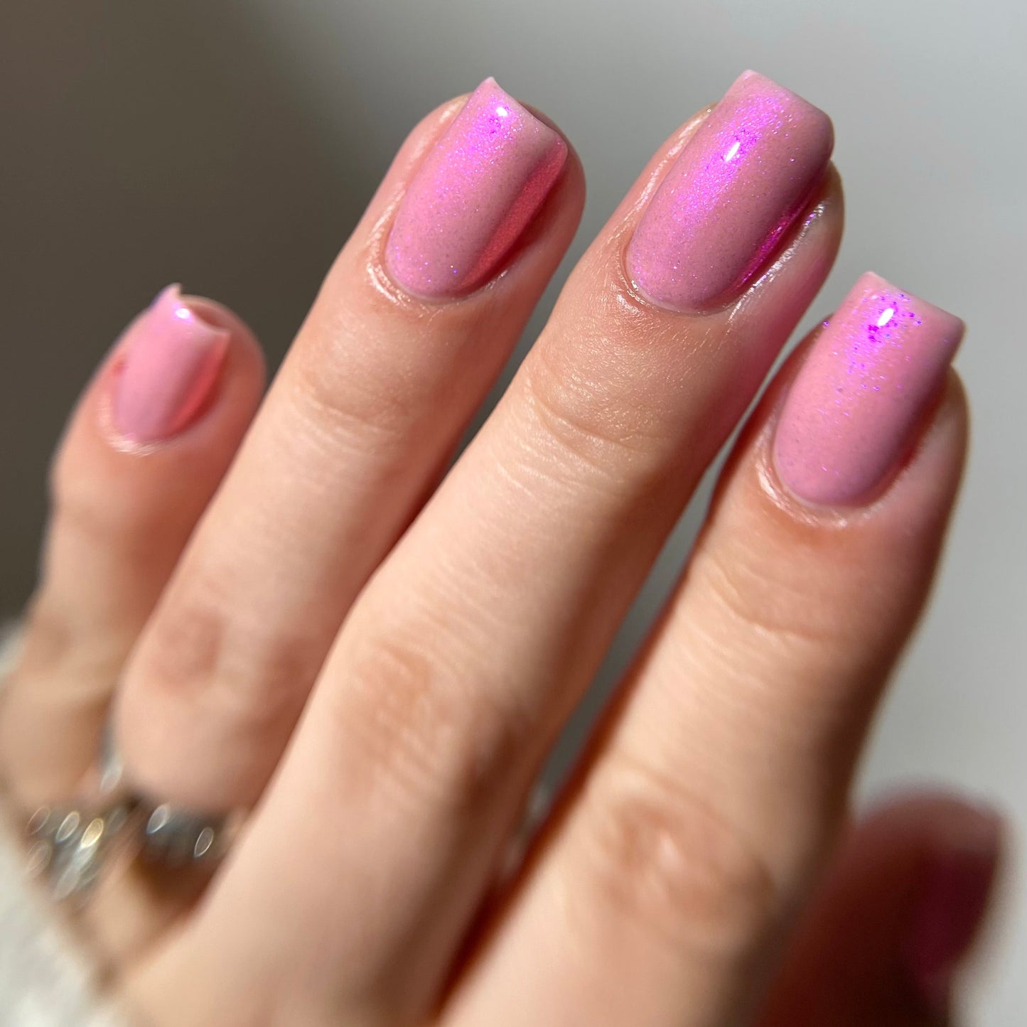 Hand with pink nail polish on a neutral background