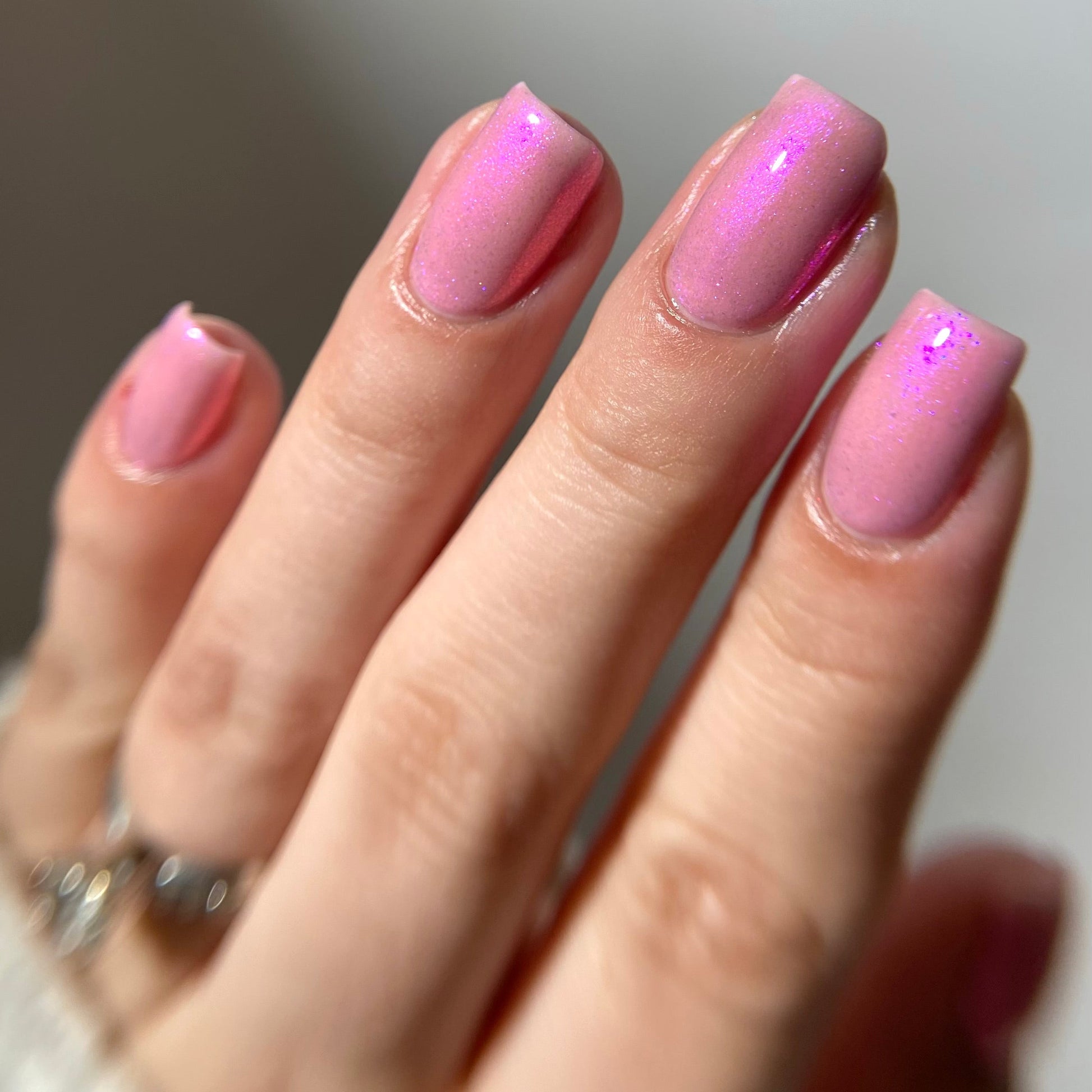 Hand with pink nail polish on a neutral background