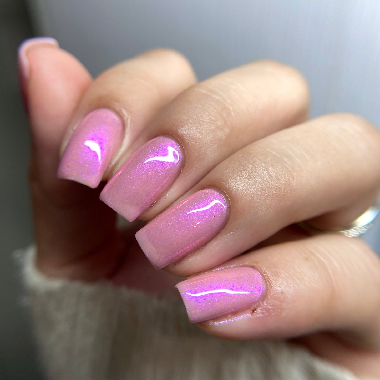 Close-up of a hand with pink nail polish on a neutral background