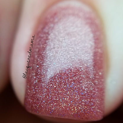 A close-up of a fingernail adorned with PI Colors' Rheum.011 Red Nail Polish—featuring a glittery, pinkish-brown hue and a 10-free formula—captures its smooth, reflective surface as it glimmers in the light. The blurred background enhances the stunning effect of this nail art.