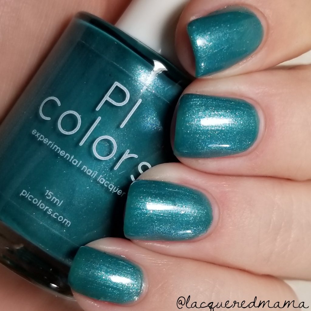 A hand with painted teal nails holds a bottle of PI Colors' PavoC.023 nail lacquer, featuring a peacock green metallic hue that shimmers brilliantly. This 10-free nail polish perfectly matches the nails. The neutral background ensures the vibrant color stands out beautifully.