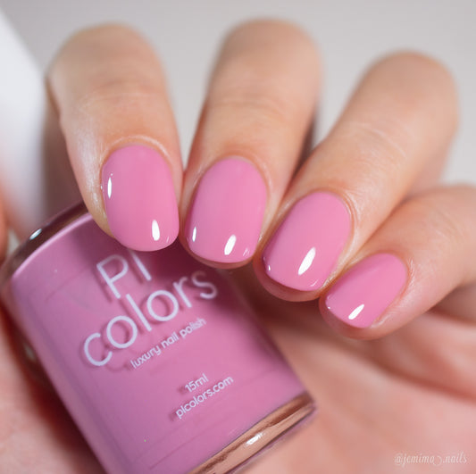 A hand with short, neatly manicured nails painted in glossy, medium pink creme nail polish holds a matching Pink Biscotti.462 bottle from PI Colors.