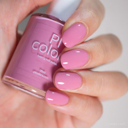 A hand with manicured nails painted in glossy brownish pink holds a matching pink bottle of handmade PI Colors nail polish labeled "Pink Biscotti.462.