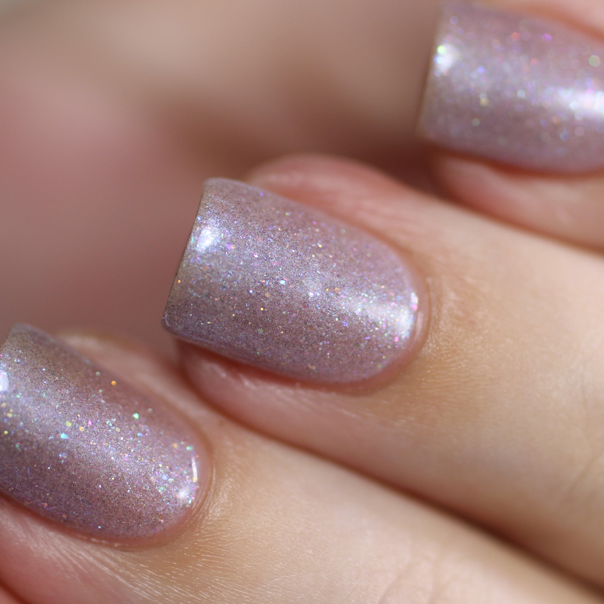 Close-up of fingers with nails painted in Snow Cherries From France.101 Purple Nail Polish by PI Colors. The nails have a glossy finish that reflects light, showcasing the holographic glitter which adds a dazzling sparkle to the purple nail polish.