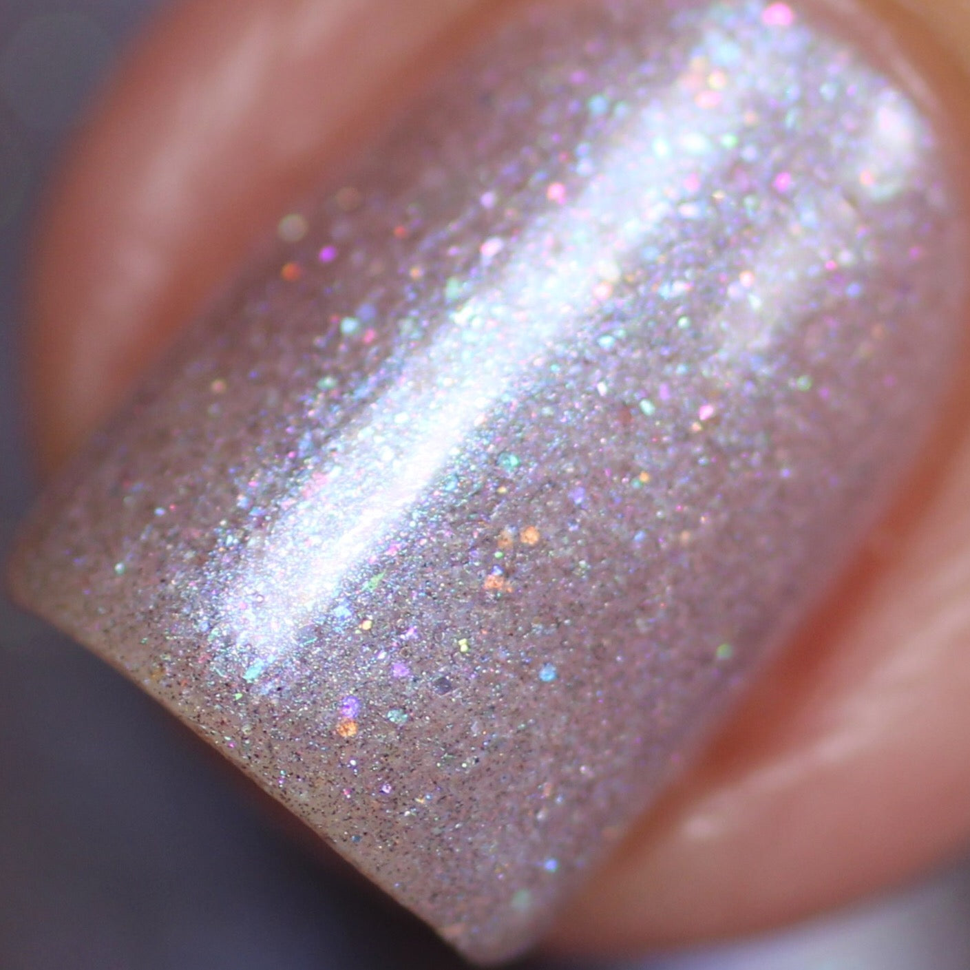 Close-up of a fingernail adorned with PI Colors' "Snow Cherries From France.101" purple nail polish. This luxurious lacquer boasts shimmering pink iridescence with tiny multicolored holographic glitter particles that elegantly reflect light. The texture is smooth, offering a glossy finish that creates a dazzling effect.