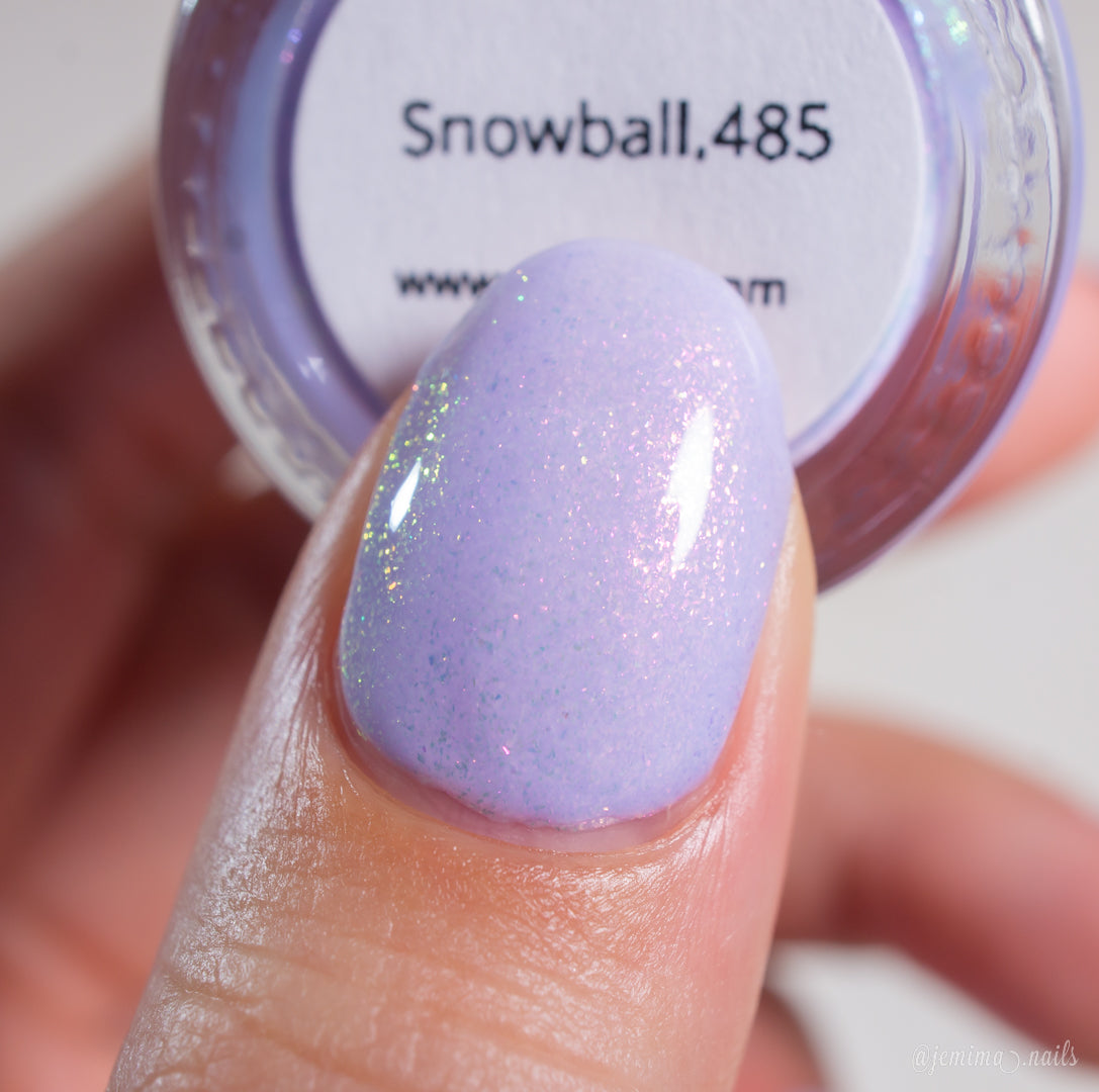 A close-up of a fingernail painted with PI Colors' handmade pastel lavender shimmer nail polish, Snowball.485, held in front of the labeled container.