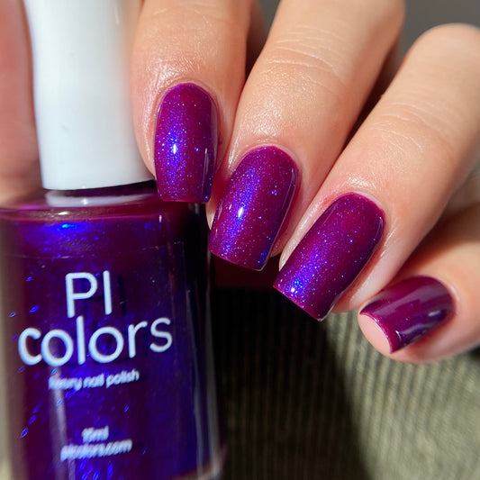 Hand with purple glittery nails holding a bottle of PI colors nail polish.