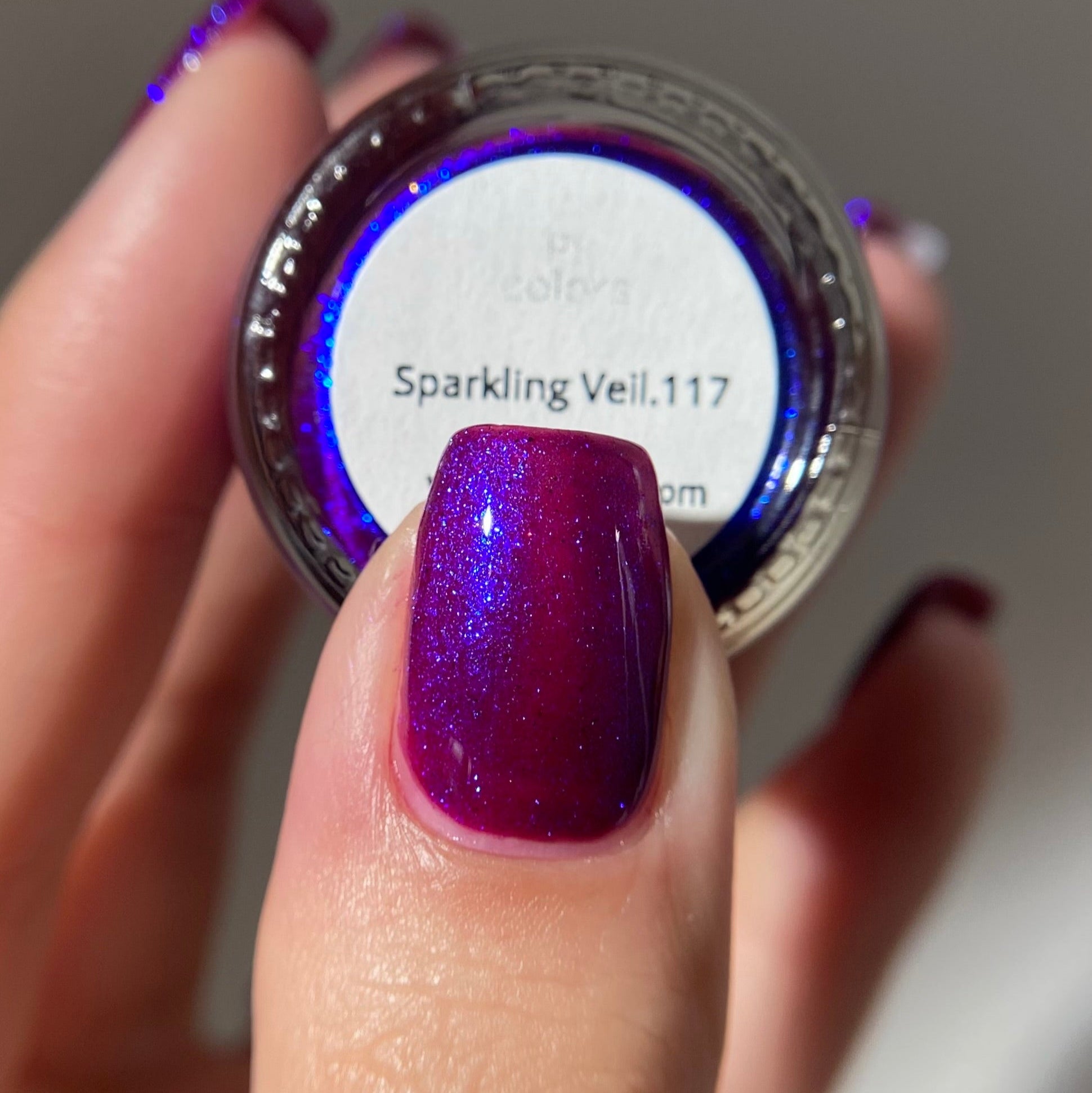 Nail polish with a sparkling effect on a finger, showing the color 'Sparkling Veil 117'.