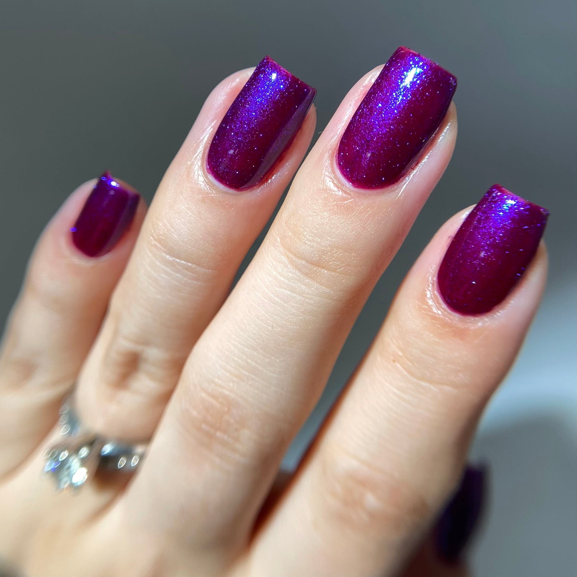 Hand with purple glittery nail polish on a neutral background