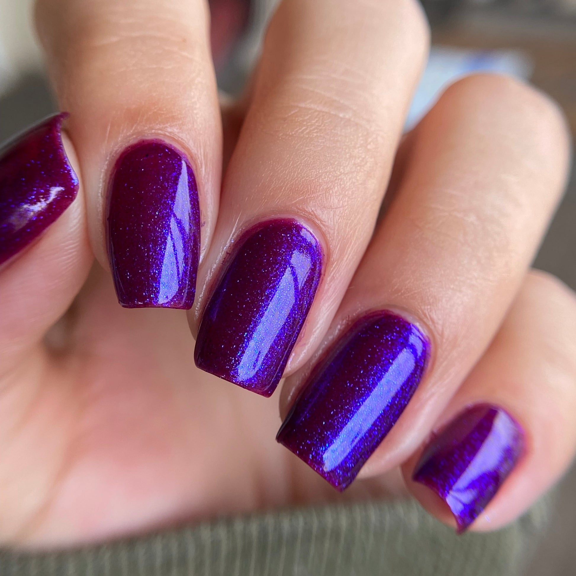 Close-up of a hand with purple glittery nail polish on a blurred background