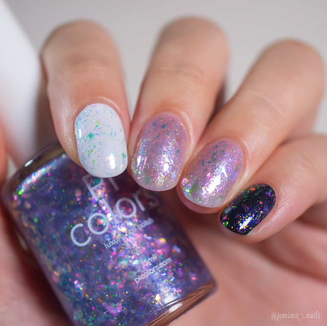 A hand displays nails painted with iridescent, flakie polishes in white, clear, and black shades while holding a PI Colors Stained Glass.436 purple glitter nail polish bottle close to the camera.