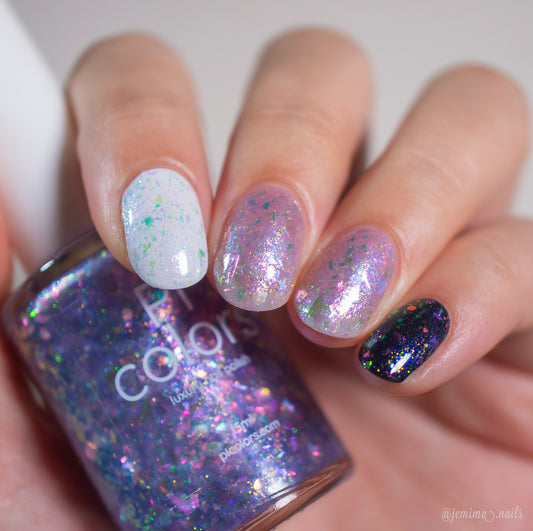 A hand displays nails painted with iridescent, flakie polishes in white, clear, and black shades while holding a PI Colors Stained Glass.436 purple glitter nail polish bottle close to the camera.
